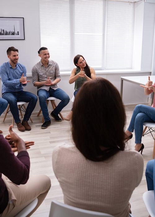 Group Of Young People Learning Deaf Gesture Sign From Woman Sitting On Chair